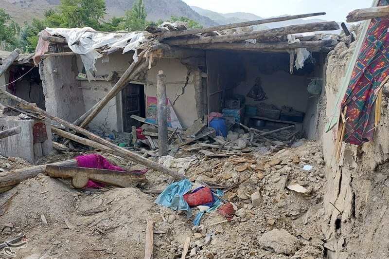 Destroyed house in Afghanistan after an earthquake, showing collapsed walls, exposed wooden beams, and debris scattered on the ground.