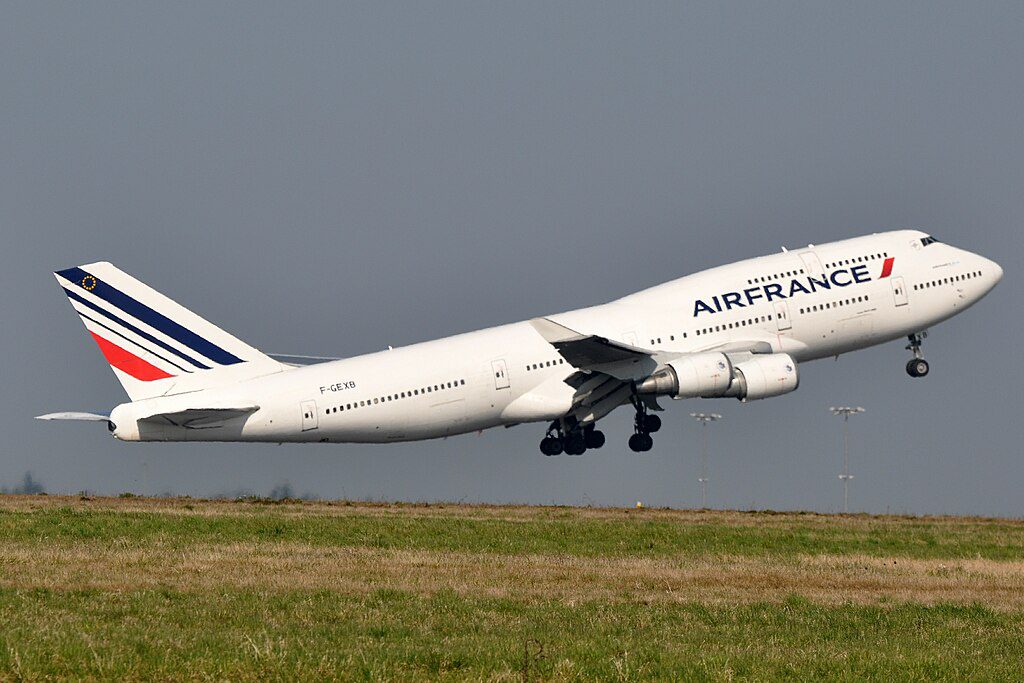 Air France Boeing 747-400M aircraft taking off from Paris-Charles de Gaulle Airport, with its distinctive red, white and blue livery visible against a cloudy sky.