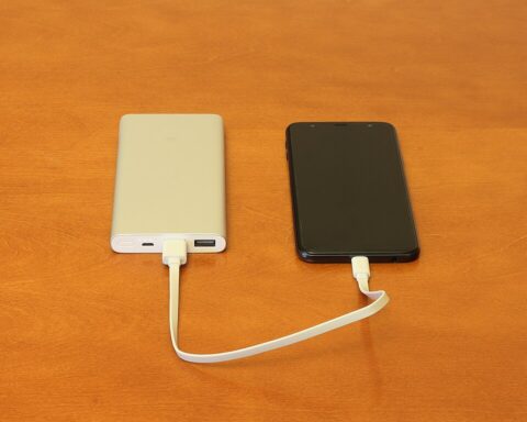 Two portable power banks - one white and one black - connected by a USB charging cable on an orange surface, similar to the recalled Anker models that pose fire hazards.