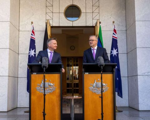 Anthony Albanese and Chris Bowen standing at podiums with microphones outside Parliament House, flanked by Australian flags, during a press event on climate policy.
