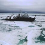 Research vessel Sikuliaq surrounded by Arctic ice floes with scientists conducting fieldwork on frozen surface during 2023 Chukchi Sea expedition to collect diatom samples from polar ice cores