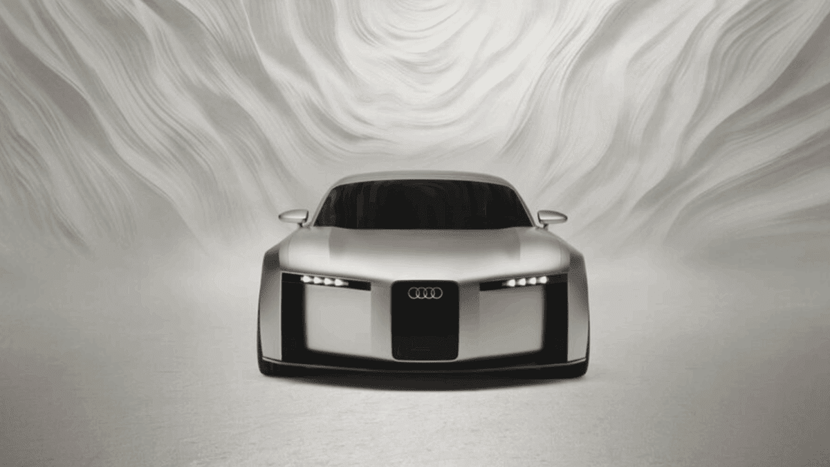 Front view of the silver Audi concept car with distinctive vertical frame grille and four-element LED headlights against a white background with flowing curved patterns.