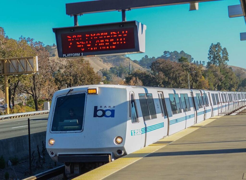 BART train pulling into Lafayette Station in California, photographed on a sunny day with hills in the background.