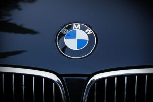 Close-up of a BMW logo emblem on the front hood of a dark blue BMW vehicle, showing the distinctive blue and white circular badge above the kidney grille.