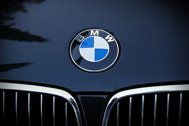 Close-up of a BMW logo emblem on the front hood of a dark blue BMW vehicle, showing the distinctive blue and white circular badge above the kidney grille.