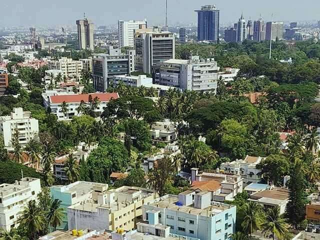 Aerial view of Bangalore skyline with high-rise buildings surrounded by dense green trees and residential areas.
