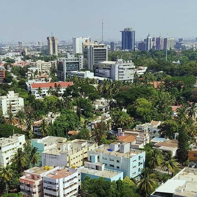 Aerial view of Bangalore skyline with high-rise buildings surrounded by dense green trees and residential areas.