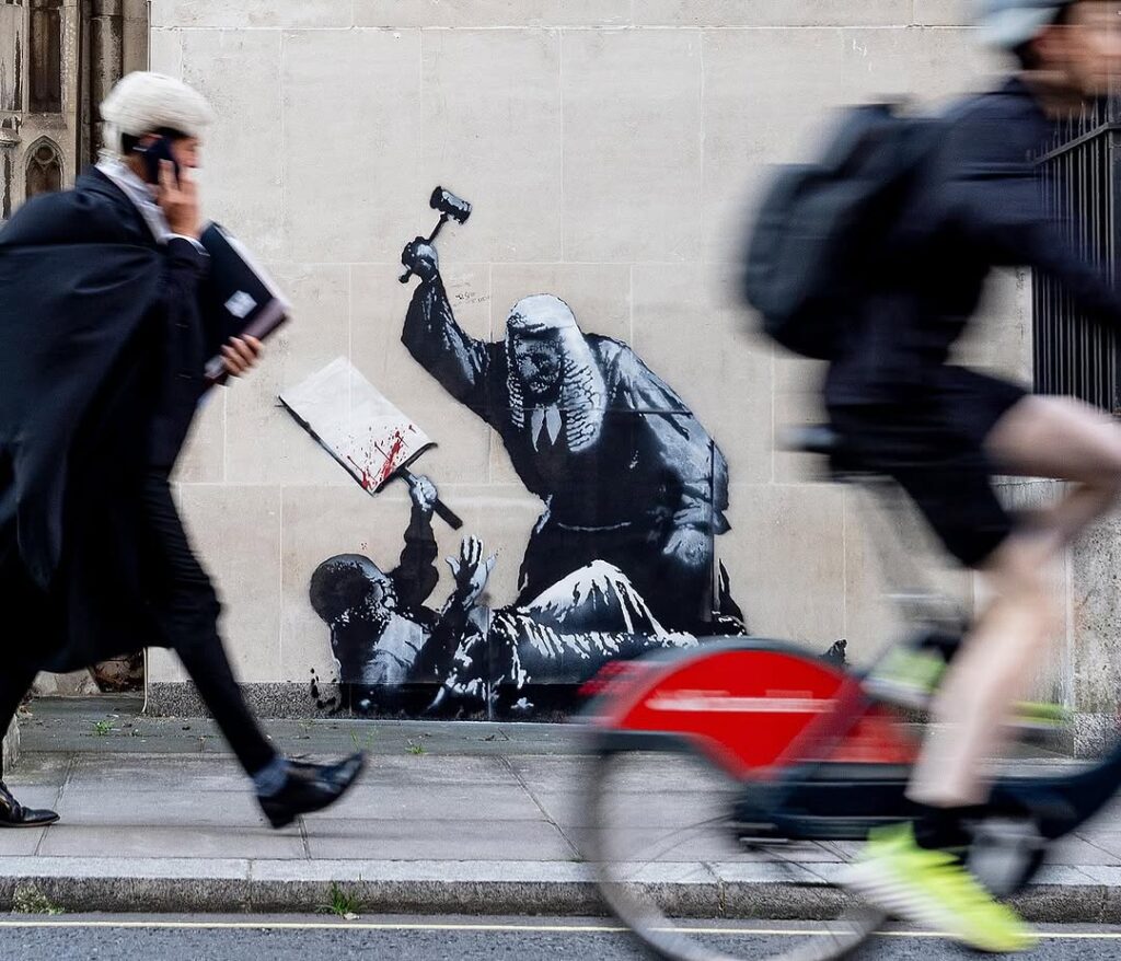 Banksy graffiti on London Royal Courts of Justice building showing judge striking protester with blood-spattered placard.