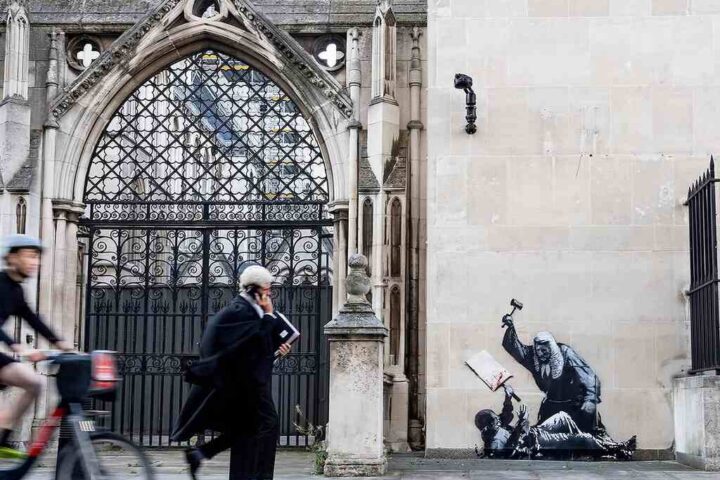 Banksy street art mural on the Royal Courts of Justice in London depicting a judge in a wig and gown striking a bloodied protester with a gavel.
