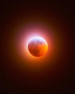 A long-exposure photograph of a total lunar eclipse, showing the moon glowing a deep, dramatic red against a starry night sky.
