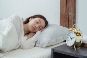 Woman sleeping peacefully in bed with white bedding next to a golden alarm clock on nightstand