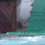Bottom trawler on the Grand Banks pulling a large green fishing net from the ocean.