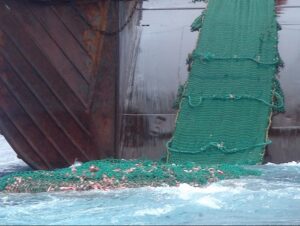 Bottom trawler on the Grand Banks pulling a large green fishing net from the ocean.