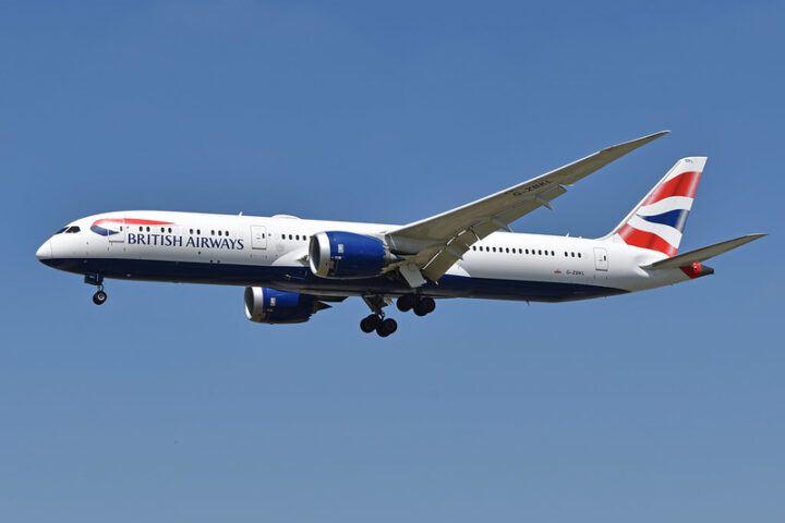 British Airways Boeing 787-9 Dreamliner with registration G-ZBKL in flight with landing gear down, featuring the airline's distinctive red, white and blue livery against a clear blue sky background