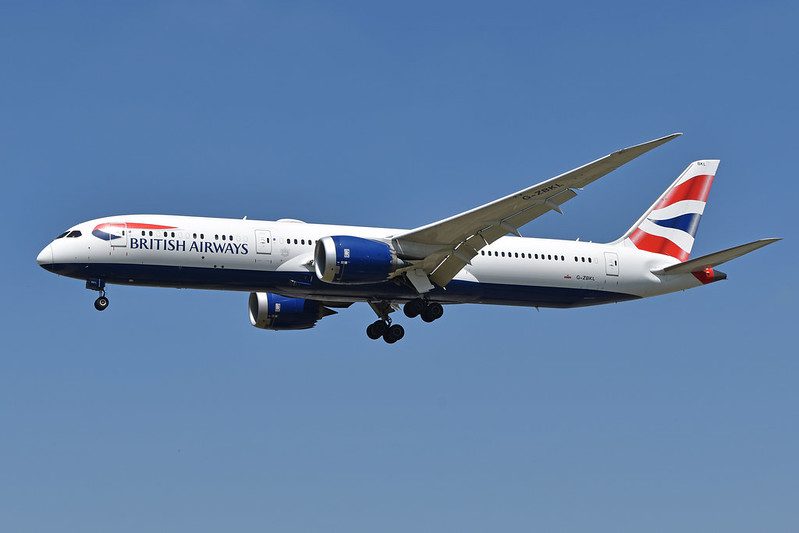 British Airways Boeing 787-9 Dreamliner with registration G-ZBKL in flight with landing gear down, featuring the airline's distinctive red, white and blue livery against a clear blue sky background