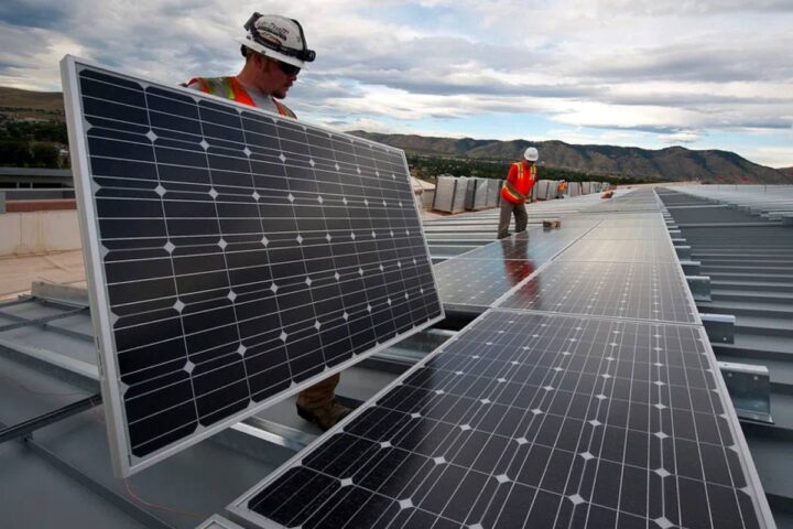 Workers installing solar panels on a commercial rooftop with mountains visible in the background.