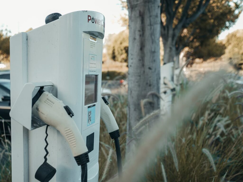 White electric vehicle charging station with charging cable attached, positioned near tall grass and trees in California