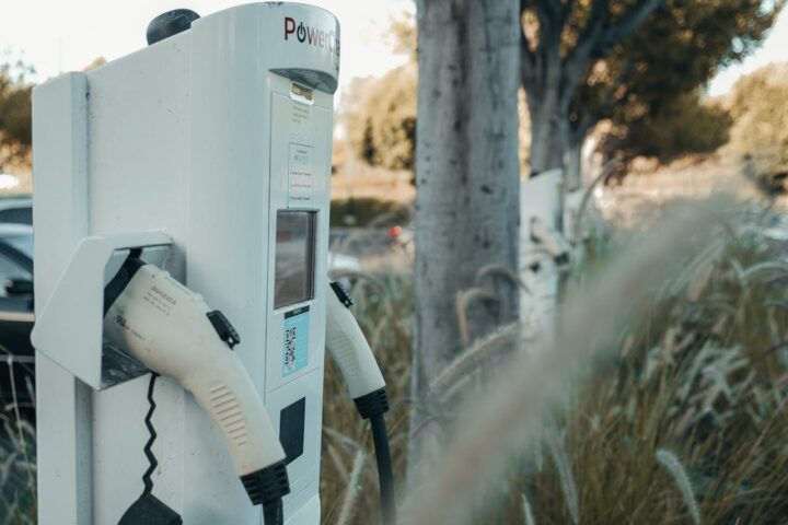 White electric vehicle charging station with charging cable attached, positioned near tall grass and trees in California