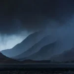 Dramatic rainfall falling over mountainous terrain with dark storm clouds, showing intense precipitation sweeping across a Scottish landscape.