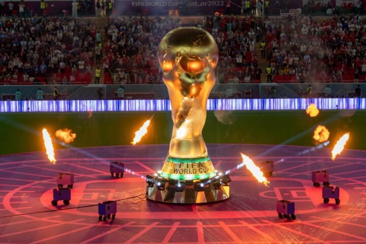 FIFA World Cup trophy on stage with fire effects during the opening ceremony in Doha, Qatar, 2022, in front of a packed stadium crowd.