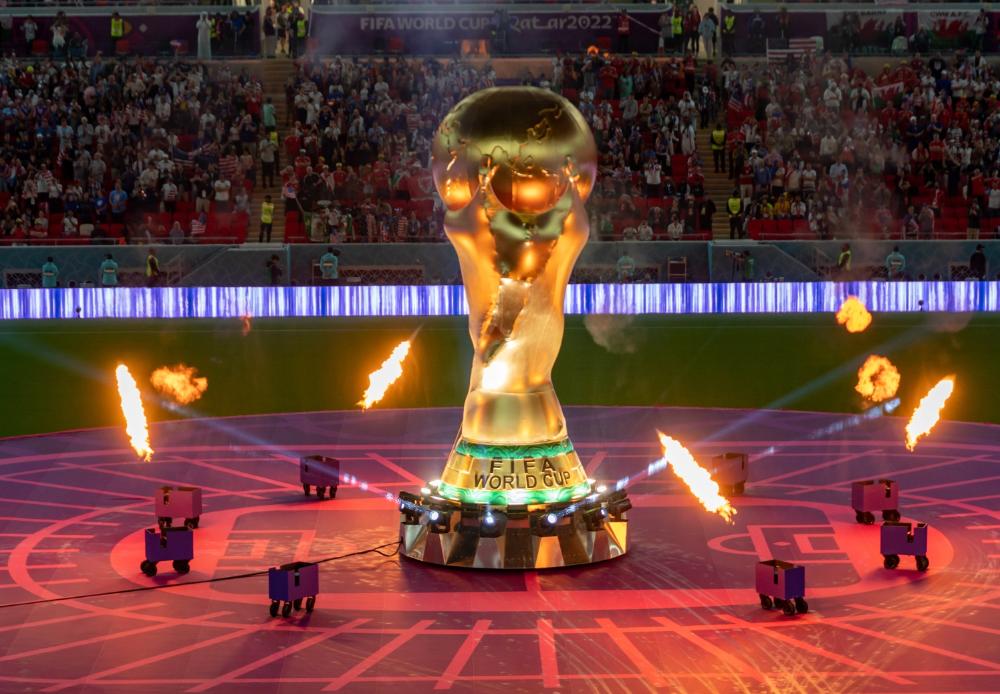 FIFA World Cup trophy on stage with fire effects during the opening ceremony in Doha, Qatar, 2022, in front of a packed stadium crowd.
