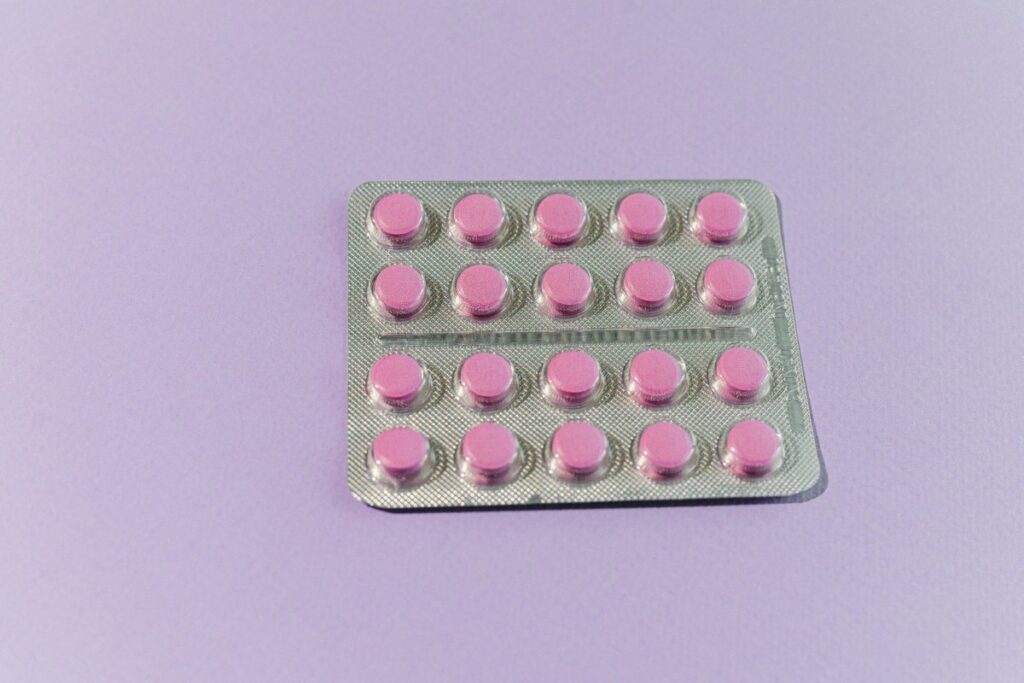 A blister pack of 20 small round pink medication tablets arranged in a grid pattern against a light purple background.