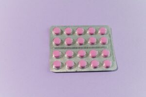 A blister pack of 20 small round pink medication tablets arranged in a grid pattern against a light purple background.