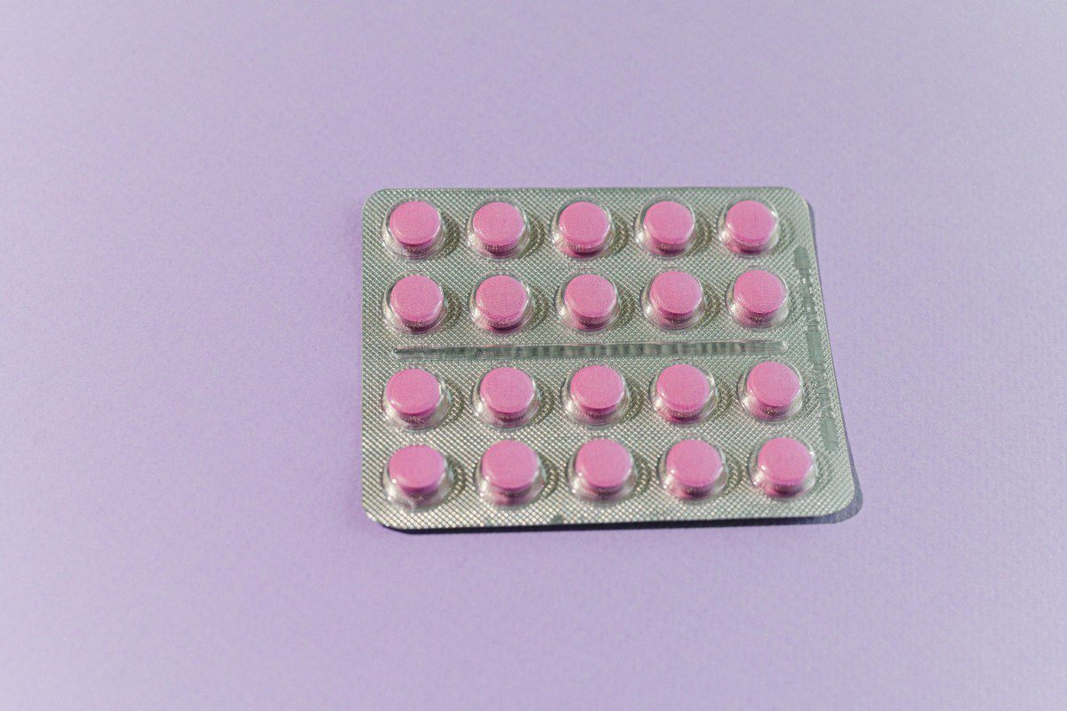 A blister pack of 20 small round pink medication tablets arranged in a grid pattern against a light purple background.