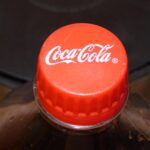 Close-up of a red Coca-Cola bottle cap on top of a plastic bottle against a dark background.