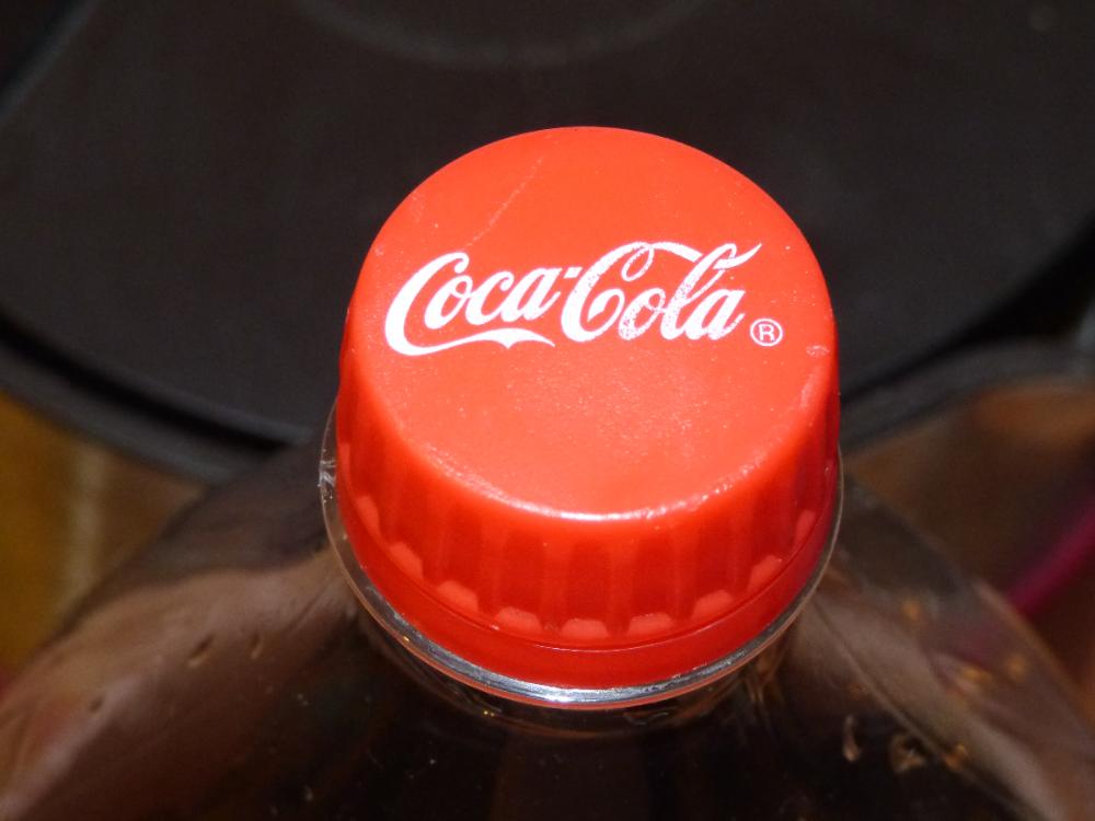 Close-up of a red Coca-Cola bottle cap on top of a plastic bottle against a dark background.