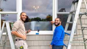Two maintenance workers installing bird-safe window film with small dot patterns on windows at the Great Swamp National Wildlife Refuge Visitor Center in New Jersey.