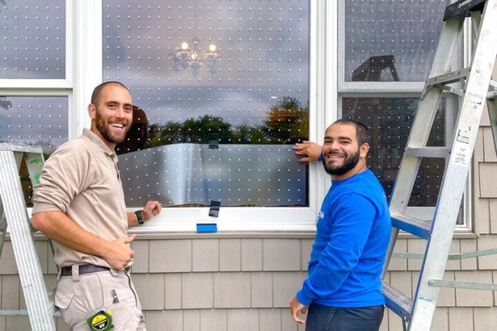 Two maintenance workers installing bird-safe window film with small dot patterns on windows at the Great Swamp National Wildlife Refuge Visitor Center in New Jersey.