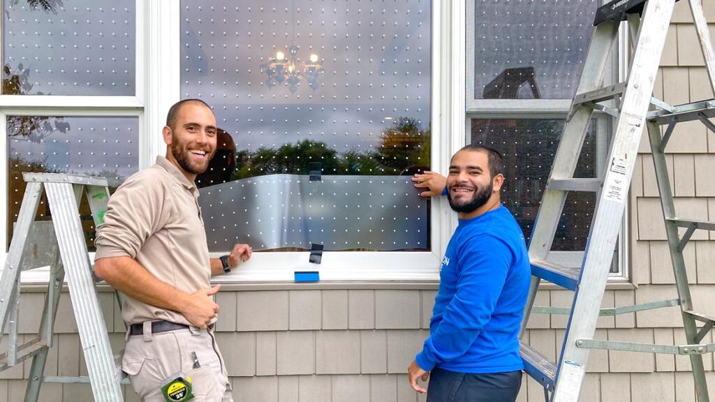 Two maintenance workers installing bird-safe window film with small dot patterns on windows at the Great Swamp National Wildlife Refuge Visitor Center in New Jersey.