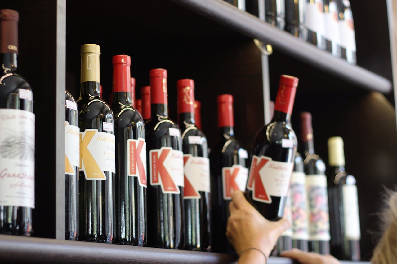 Row of Kirkland wine bottles with K logo on shelves with a person's hand reaching for one bottle