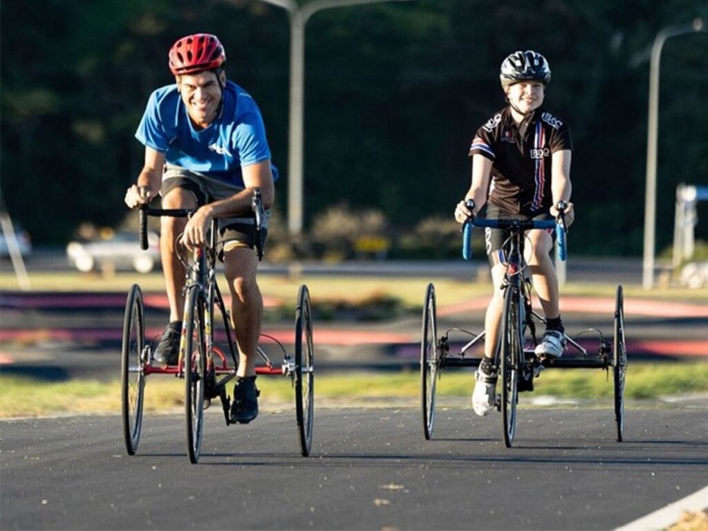 Two cyclists on adaptive bikes riding outdoors, representing community-focused health and sustainability initiatives supported by the Bupa Foundation.