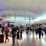 Main terminal at Dallas Love Field Airport showing the interior concourse with travelers walking through the bright, modern space featuring distinctive ceiling lighting installation.