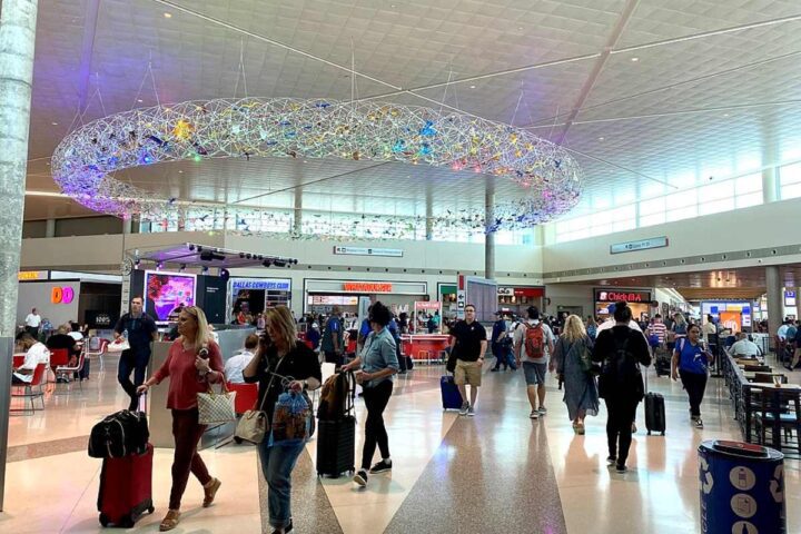 Main terminal at Dallas Love Field Airport showing the interior concourse with travelers walking through the bright, modern space featuring distinctive ceiling lighting installation.