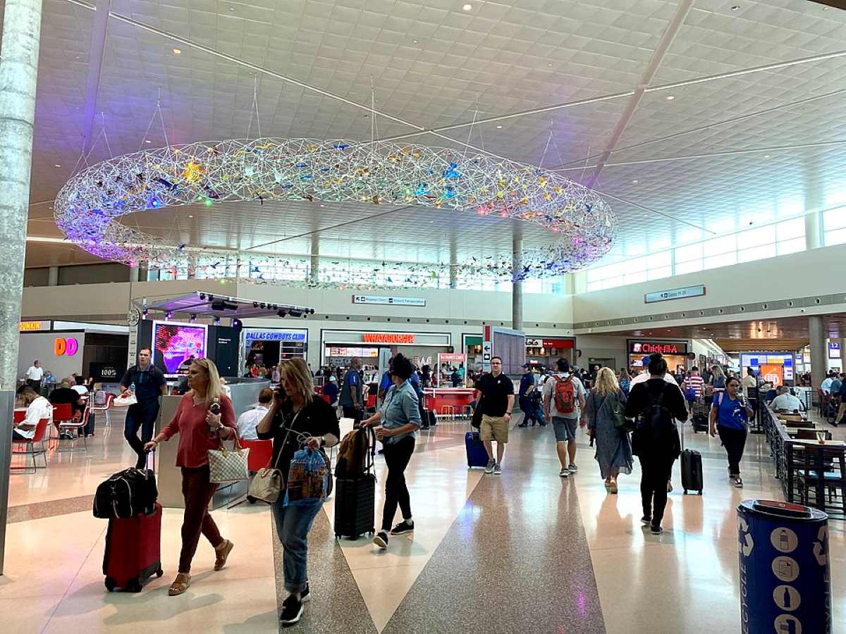 Main terminal at Dallas Love Field Airport showing the interior concourse with travelers walking through the bright, modern space featuring distinctive ceiling lighting installation.