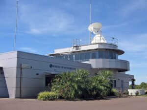 The Bureau of Meteorology’s Darwin Airport Met Office building featuring a white radar dome, rooftop antennas and surrounding palm trees under a clear blue sky