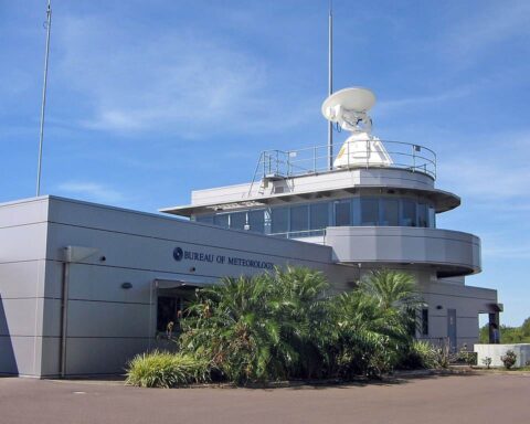 The Bureau of Meteorology’s Darwin Airport Met Office building featuring a white radar dome, rooftop antennas and surrounding palm trees under a clear blue sky