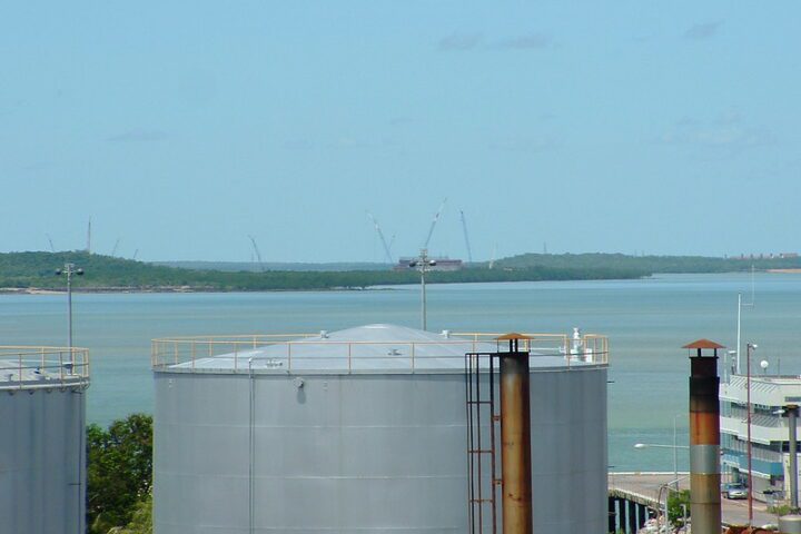 Aerial view of the Darwin LNG gas plant at Wickham Point under construction in 2004, with fuel tanks in the foreground and cranes against the skyline.