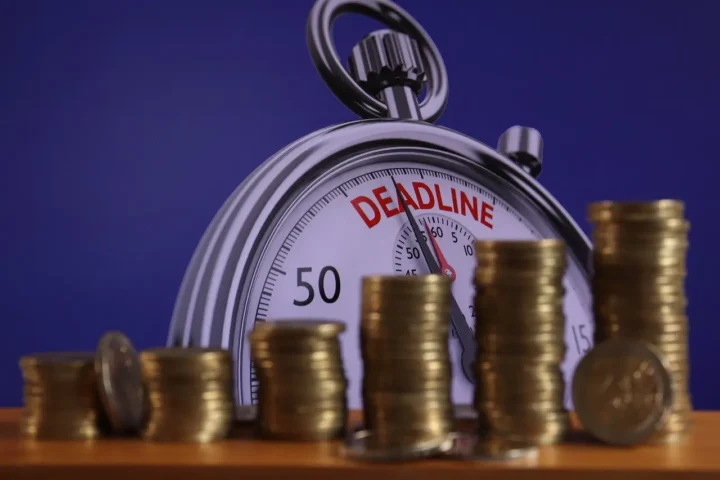 Stopwatch showing the word deadline with stacked coins symbolizing financial pressure and repayment urgency.