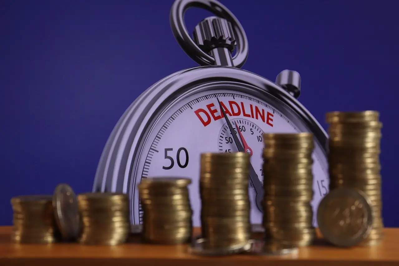Stopwatch showing the word deadline with stacked coins symbolizing financial pressure and repayment urgency.