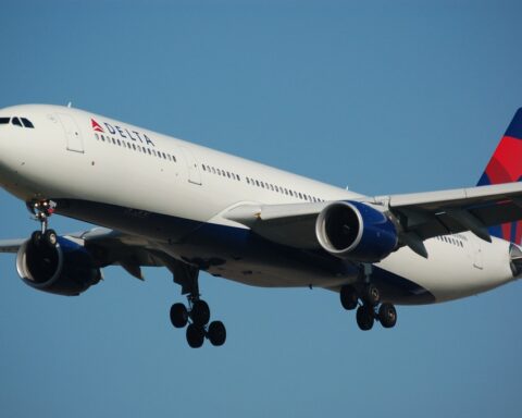 Delta Air Lines passenger aircraft with white fuselage and blue engines preparing to land with landing gear deployed against a blue sky background.