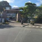 Front view of Directorate of Health Services building in Kerala with trees, vehicles, and clear sky.