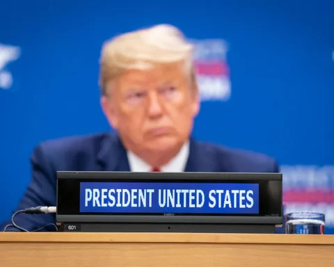 Donald Trump blurred in background with a conference placard reading “President United States” in focus, captured at an international session.
