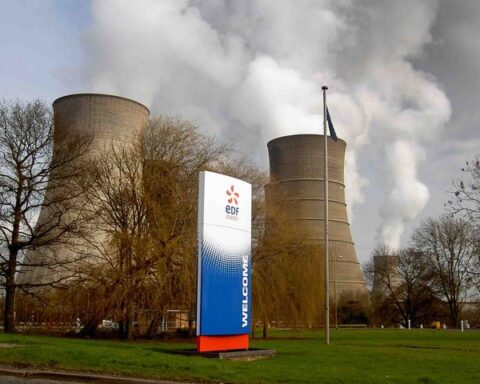 Cooling towers at an EDF power station with trees in the foreground against a blue sky background.