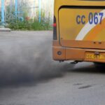 Black exhaust smoke billowing from a yellow bus with license plate CC 067 against a gray road surface