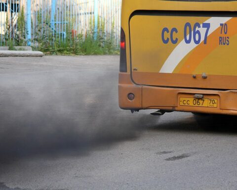 Black exhaust smoke billowing from a yellow bus with license plate CC 067 against a gray road surface