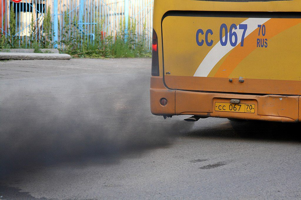 Black exhaust smoke billowing from a yellow bus with license plate CC 067 against a gray road surface